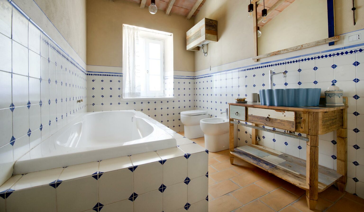 Vista totale di uno dei bagni in legno di un casale antico in Val D'Orcia. Il mobile bagno è in legno massello di recupero colorato e color naturale. In primo piano parte di una vasca da bagno