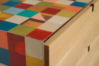 Dettaglio della cassettiera multicolore con struttura in legno multistrato, rivestimento con mosaico di tessere di legno decorate con microcemento colorato. ante e gambe in legno massello di rovere. la cassettiera dispone di 5 cassetti.