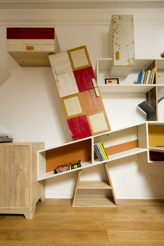 arredo contemporaneo, particolare di parete attrezzata in legno di recupero bianco, rosso e giallo con moduli incastrati l'uno sull'atro in equilibrio instabile