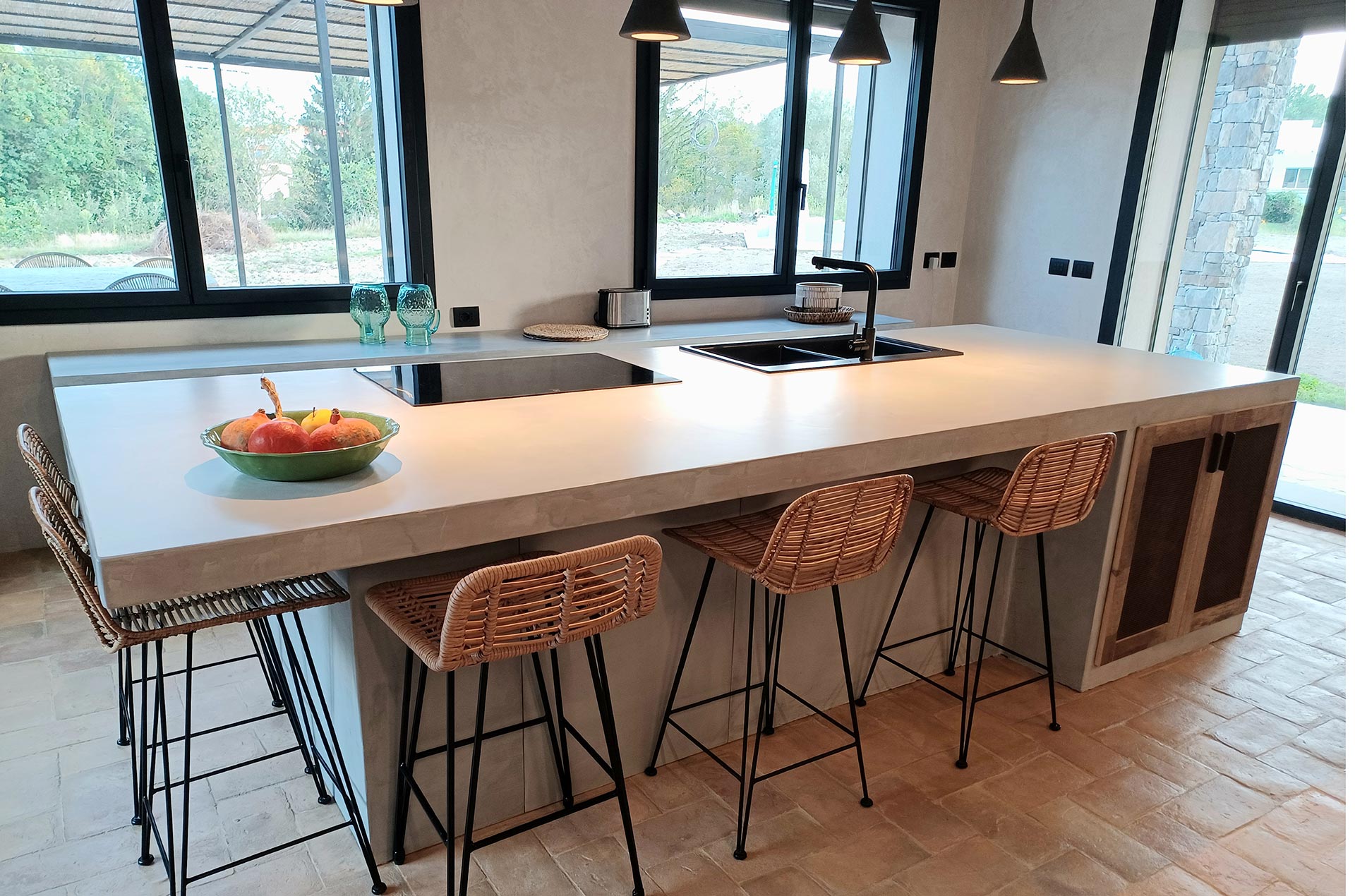 Vista totale id un ambiente openspace cucine moderne con isola con grande tavolo in legno e sedie nere moderne e bancone cucina in microcemento grigio e ante in legno di recupero naturale grezzo